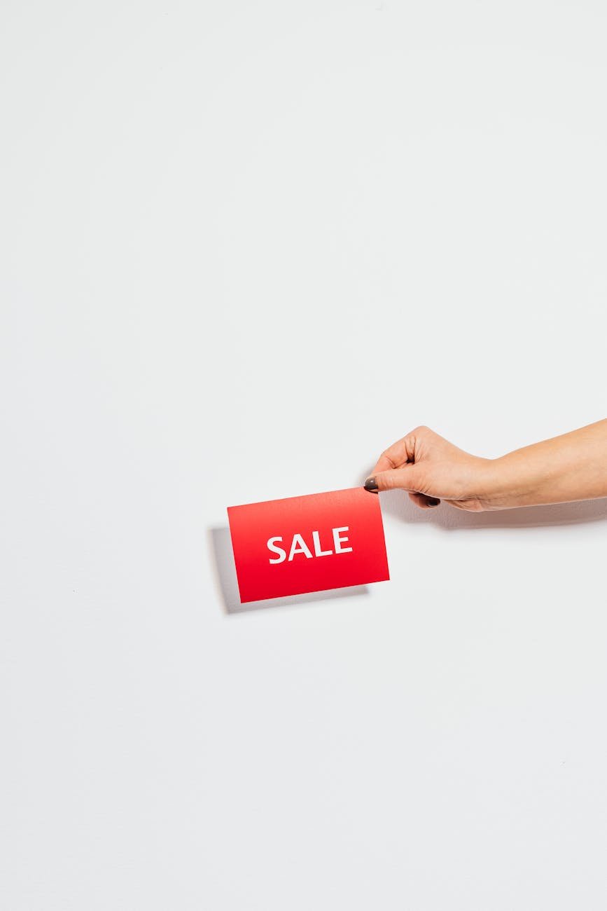 Hand holding a red 'Sale' card against a white background. Perfect for promotions.